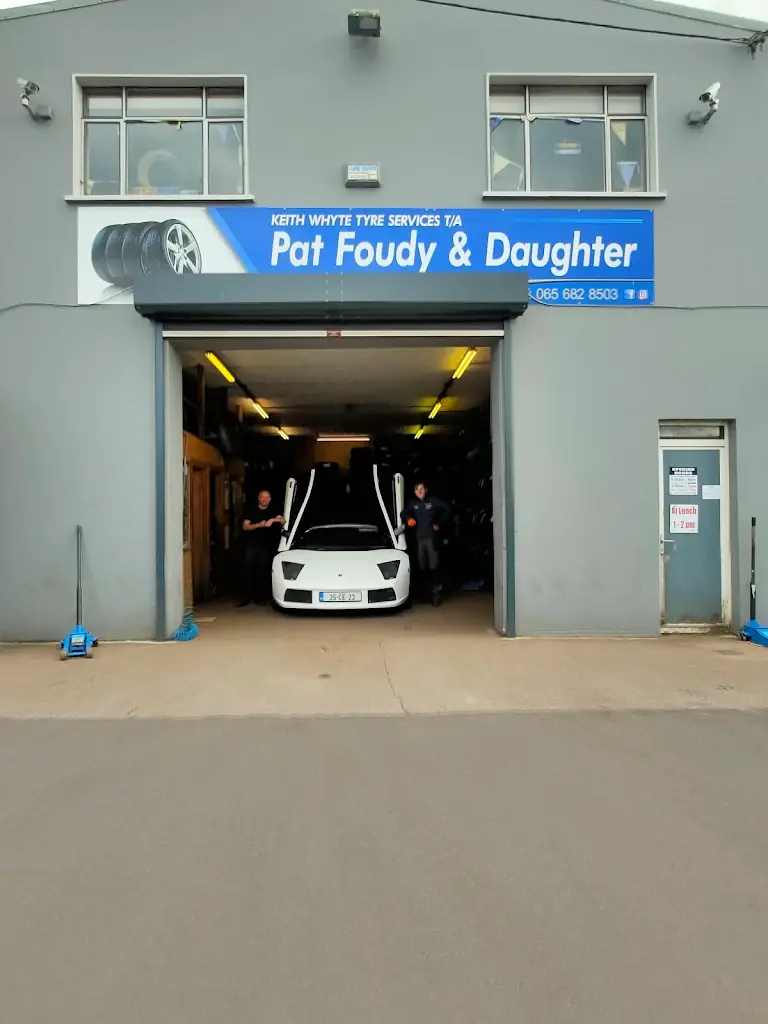 Two of the team standing beside a white Lamborghini with its doors up in the Pat Foudy and Daughter tyre bay